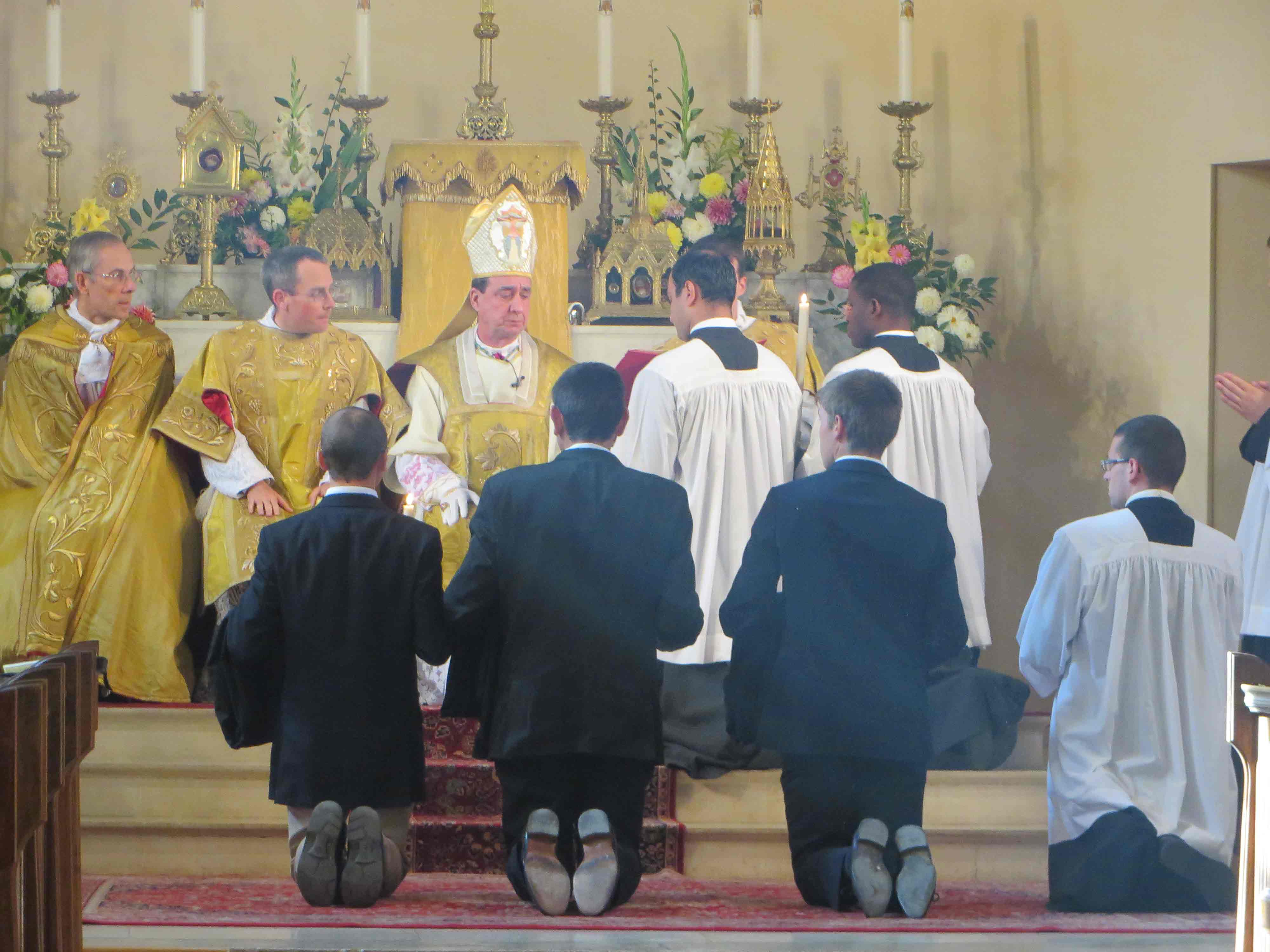 i tre fratelli inginocchiati davanti al vescovo per la benedizione delle talari
